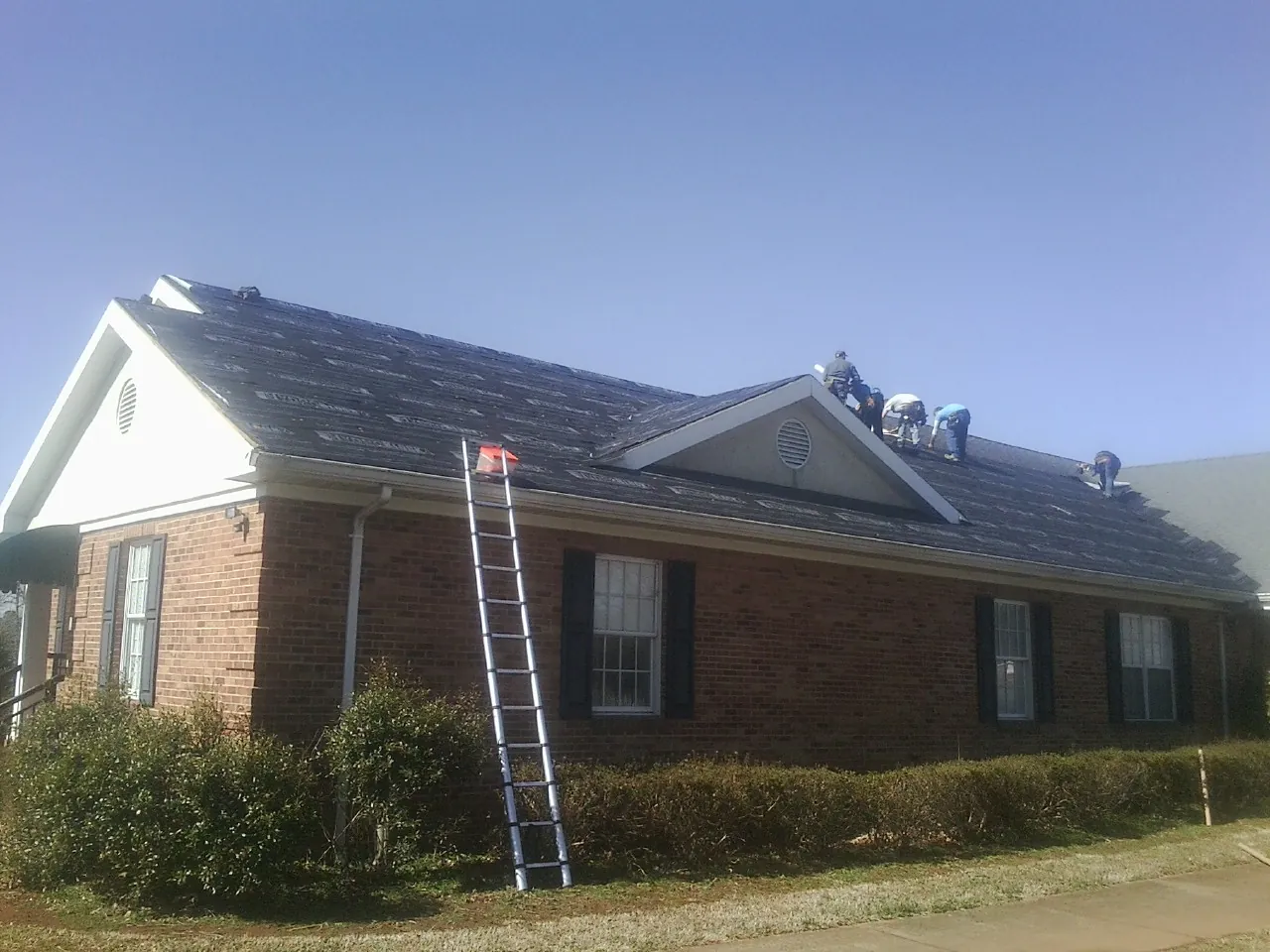 Crew tearing shingles off a brick ranch roof with a ladder set — Emergency Roof Repair work by our crew in La Center