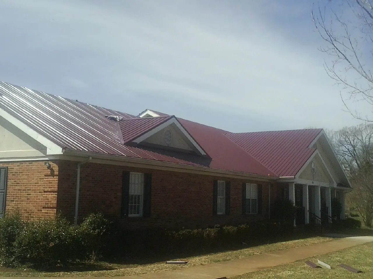 Red metal roof with gabled entries on a long brick building, from a Hail Damage Roof Repair job in La Center