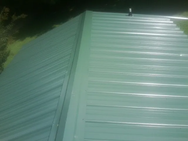 New green metal panels meeting at the ridge of a roof — Flat Roof Repair work by our crew in La Center