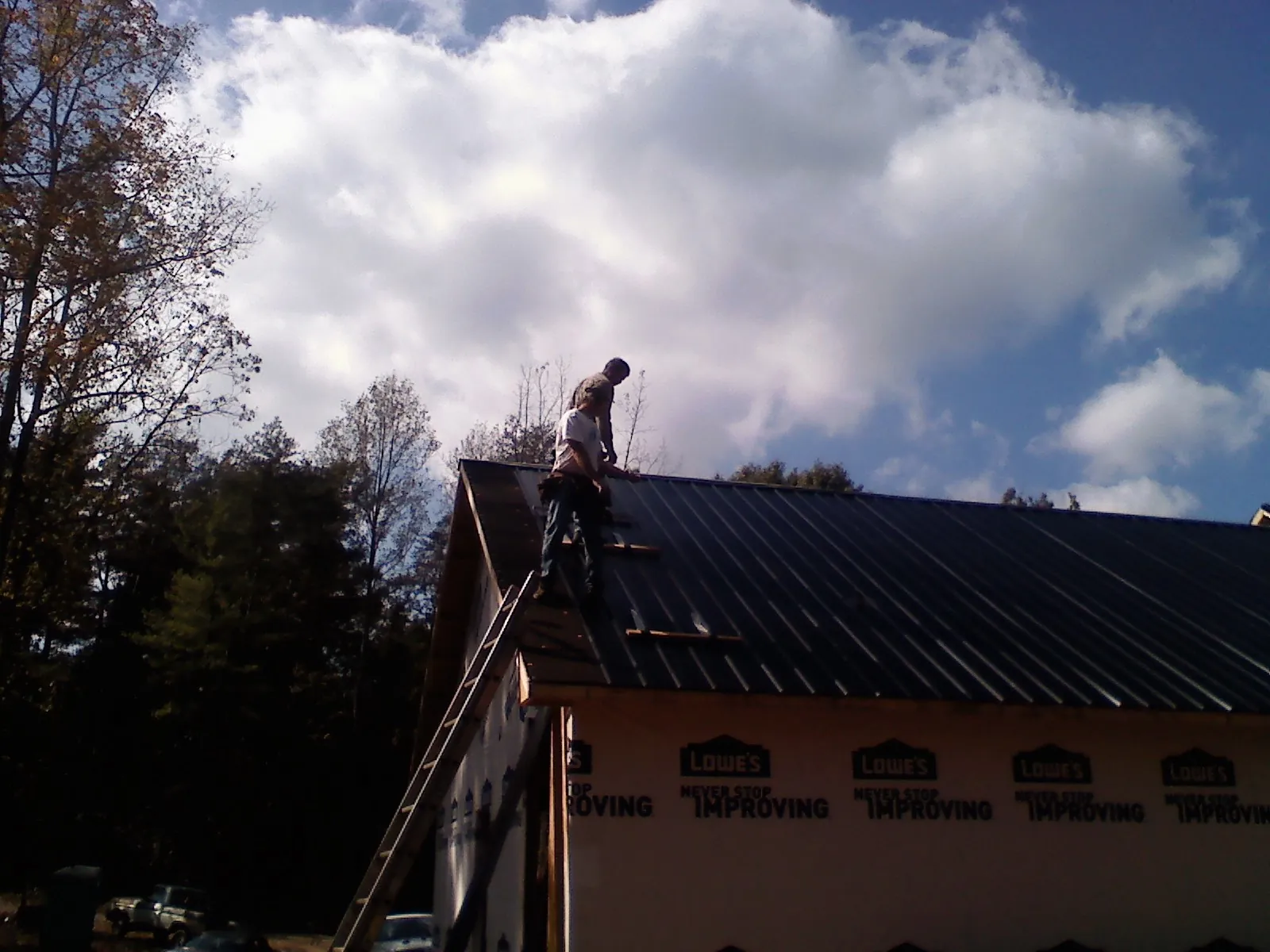 Roofer fastening dark metal panels high against a cloudy sky, from a Roof Inspection job in La Center