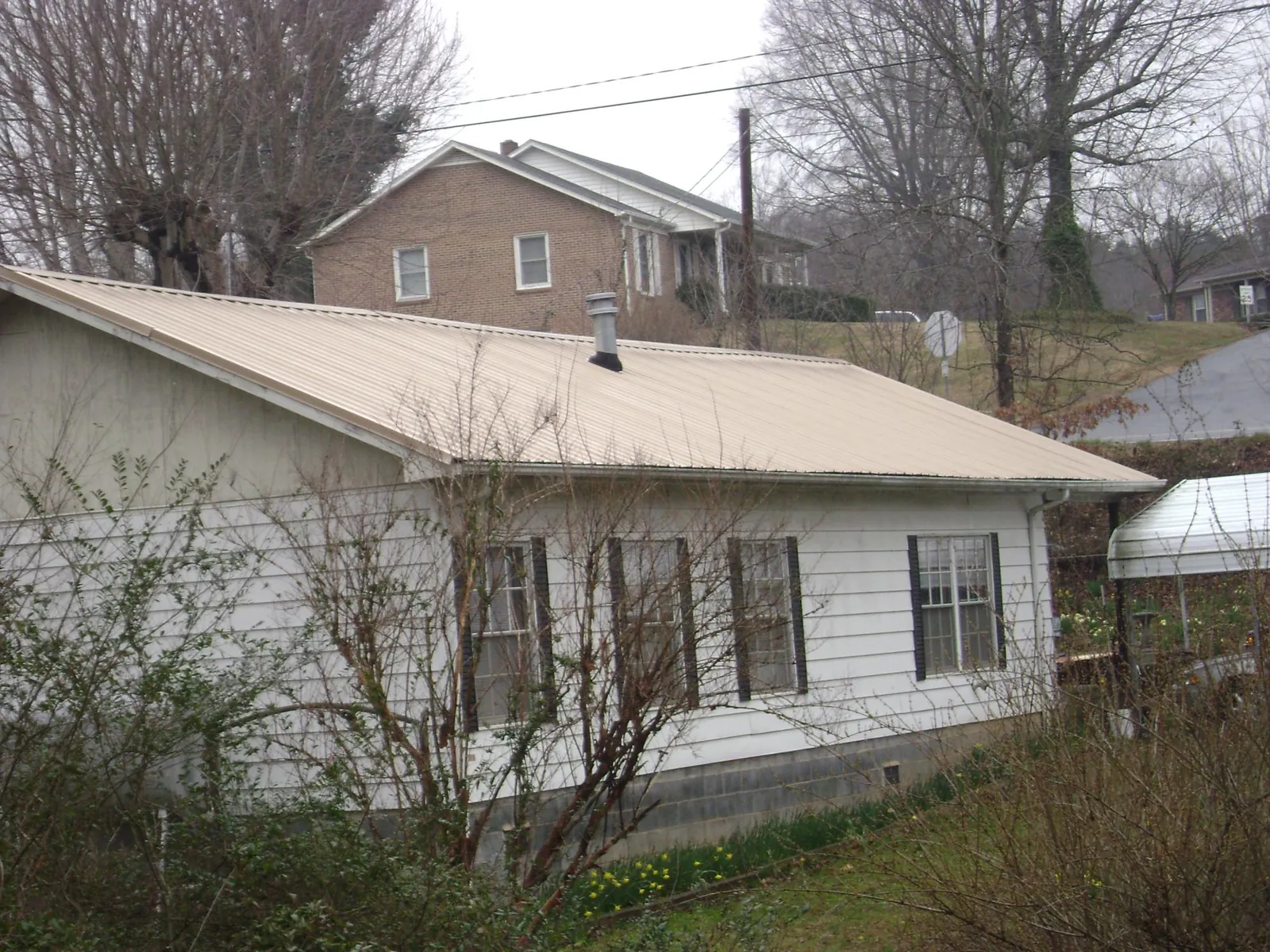 Tan metal roof on a white sided house set into a hillside — Commercial Roofing by Roofing Brothers in La Center